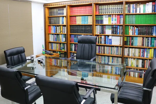 Sala de reuniões do escritório, com mesa de vidro e estantes de livros