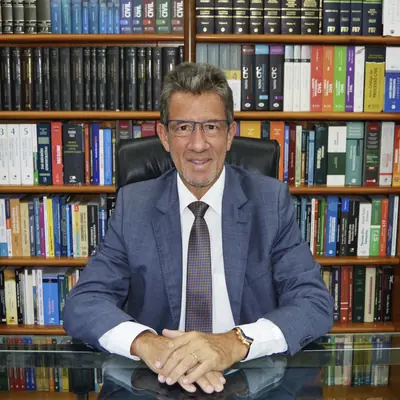 Sérgio Nogueira Furtado de Lemos, sentado à mesa diante da estante de livros do escritório